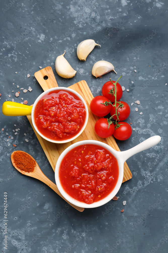 Bowls with tasty tomato sauce and fresh vegetables on blue background