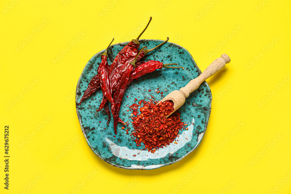 Plate with dry chili and ground  peppers on yellow background