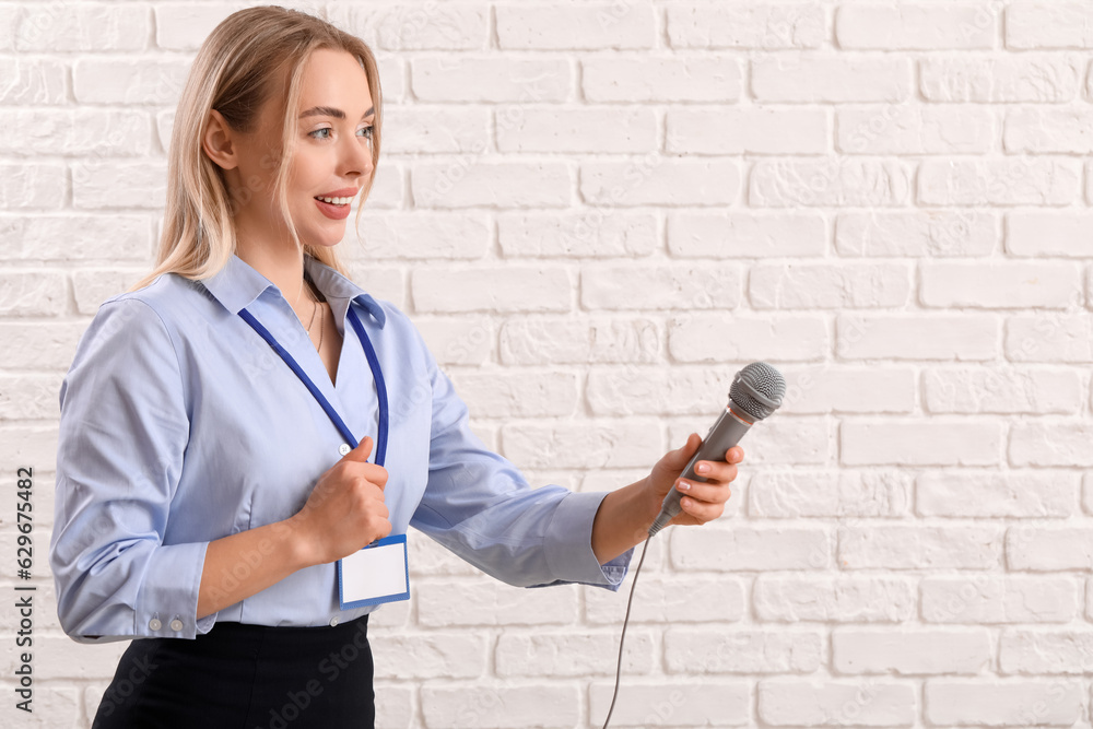 Female journalist with microphone on white brick background