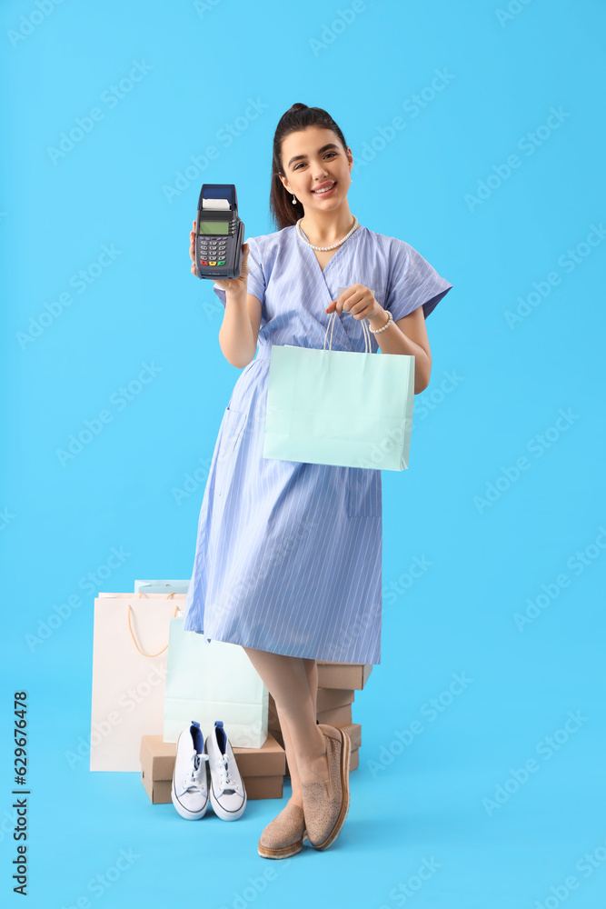 Young woman with shopping bag and payment terminal on blue background