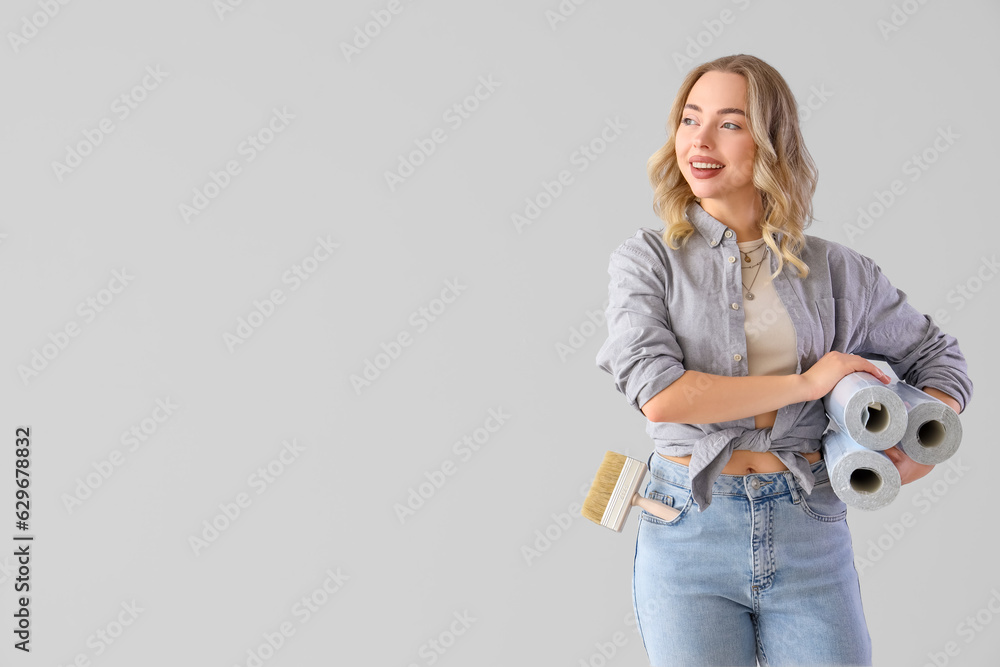 Young woman with wallpaper rolls on grey background