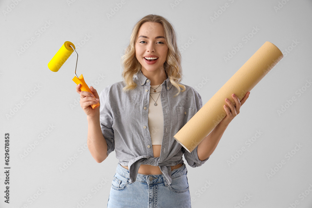 Young woman with wallpaper roll and brush on grey background