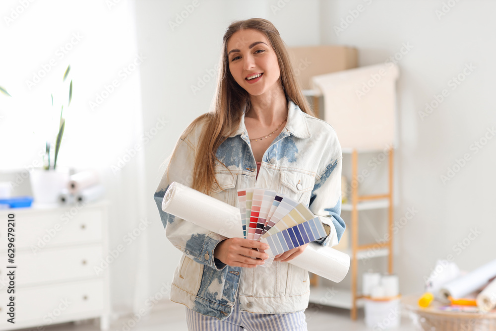 Young woman with wallpaper roll and color palettes at home