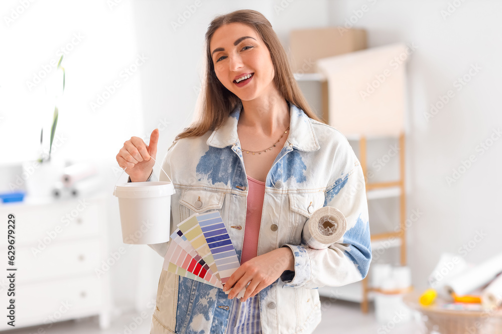 Young woman with wallpaper, glue and color palettes at home