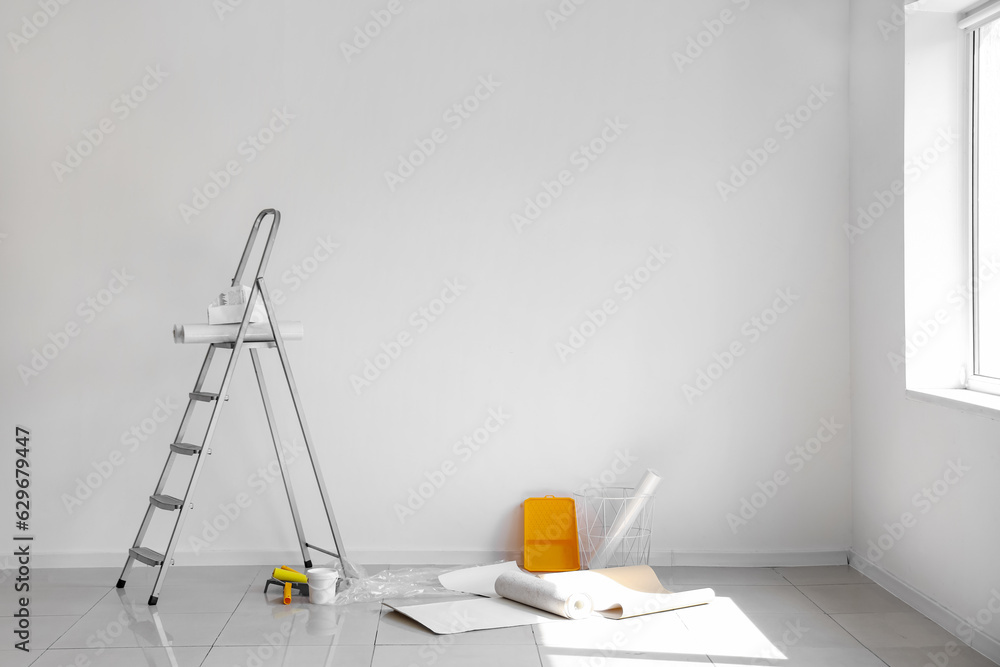 Wallpaper rolls with supplies and ladder in light room