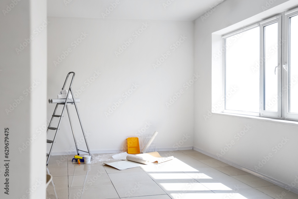 Wallpaper rolls with supplies and ladder in light room