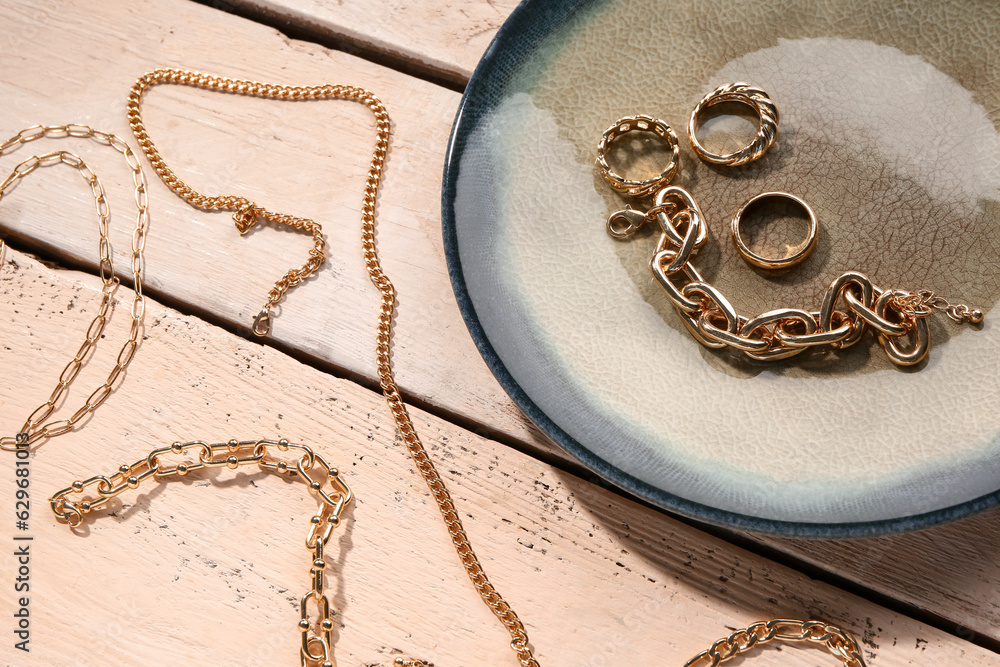 Plate with beautiful golden jewellery on wooden background