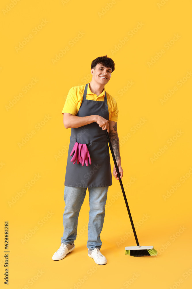 Male janitor with broom on yellow background