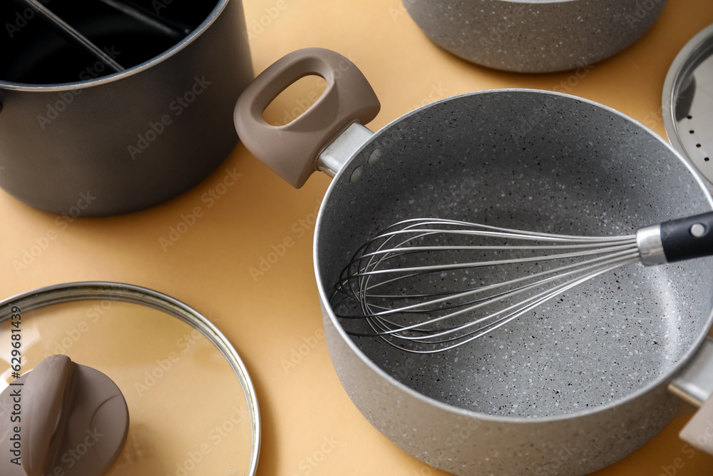 Cooking pot and whisk on beige background, closeup