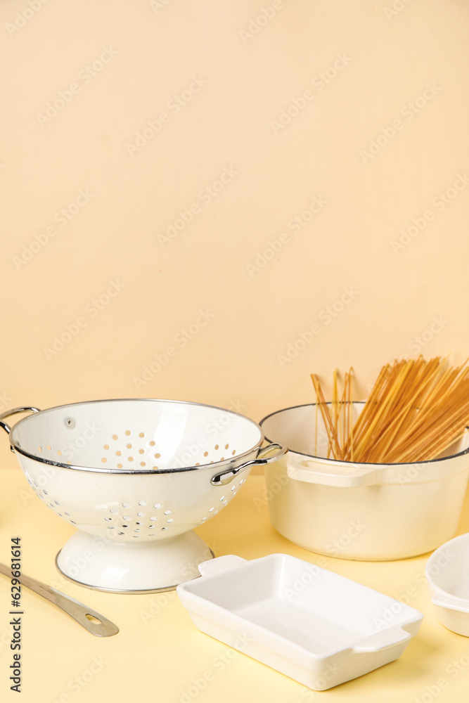 Set of kitchen utensils and pot with raw pasta on beige background