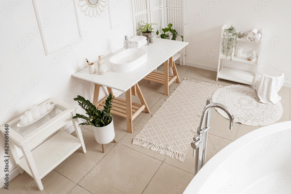 Interior of light bathroom with white sink, bathtub and houseplants