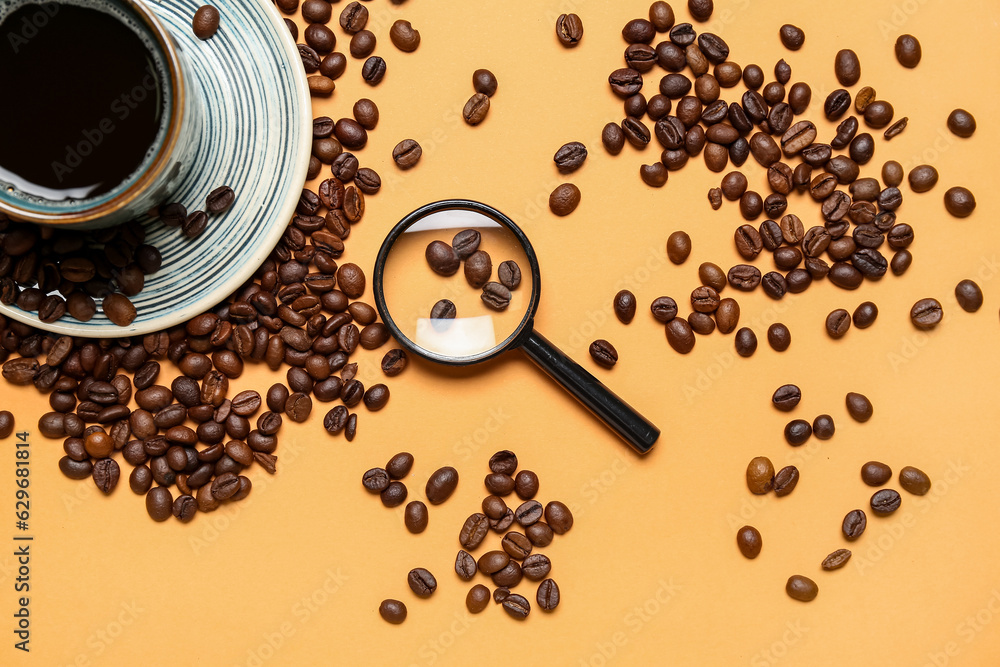 Magnifier and cup of coffee with beans on pale orange background