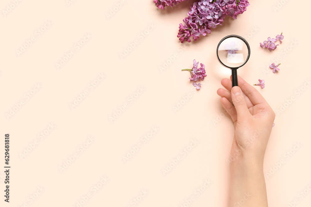 Female hand with magnifier and beautiful lilac flowers on pale pink background