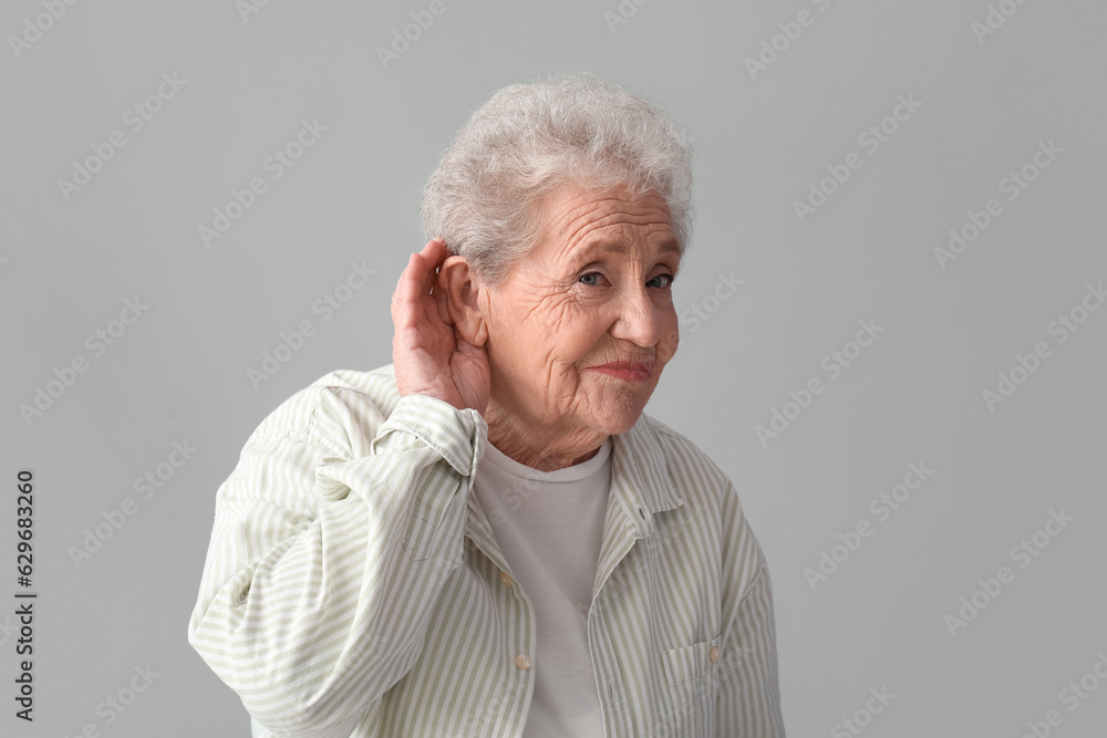 Senior woman trying to hear something on grey background