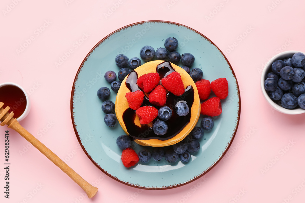 Plate with sweet pancakes and berries on pink background