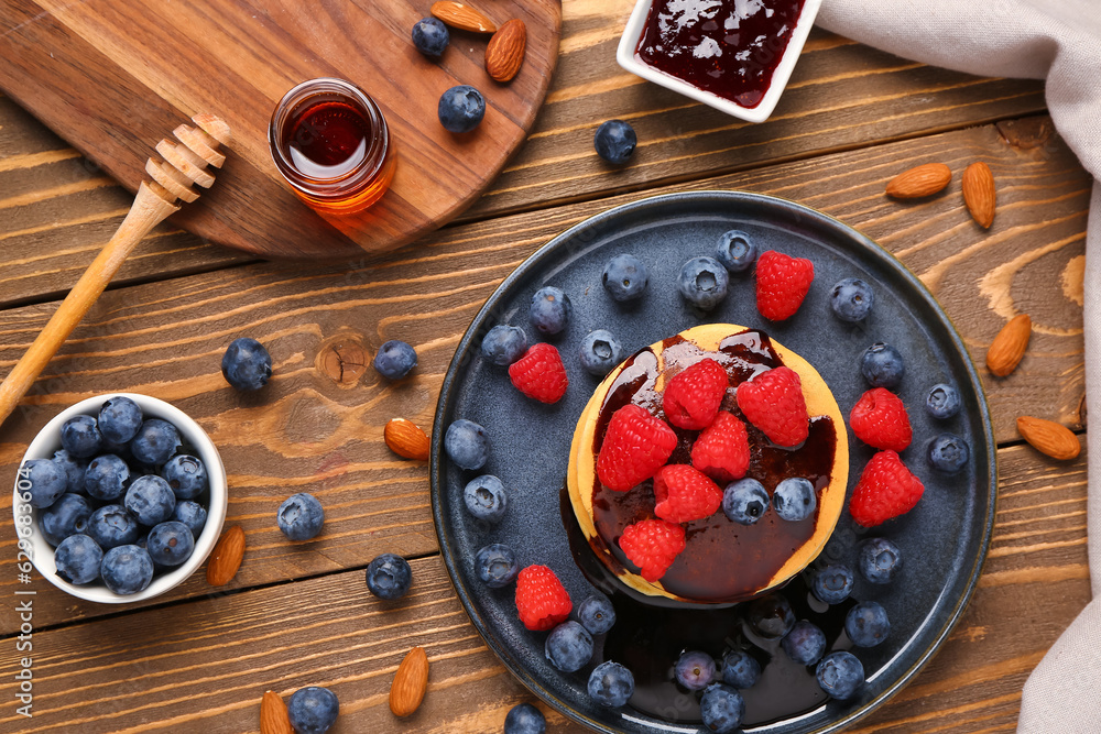 Plate with sweet pancakes, berries, nuts and jam on wooden background