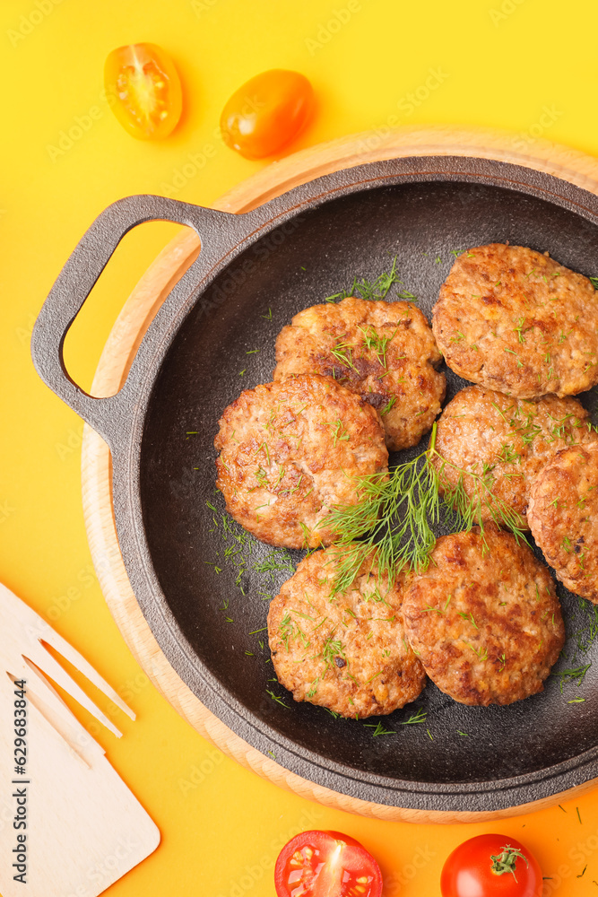 Frying pan with cutlets, dill and tomatoes on yellow background