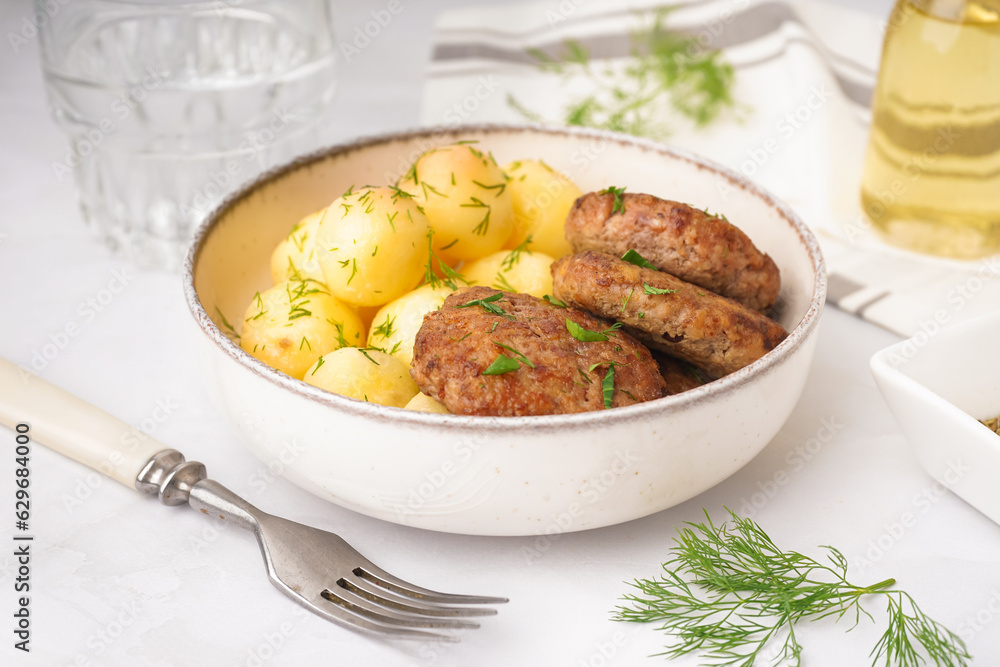 Bowl with cutlets, boiled baby potatoes and dill on white table in kitchen