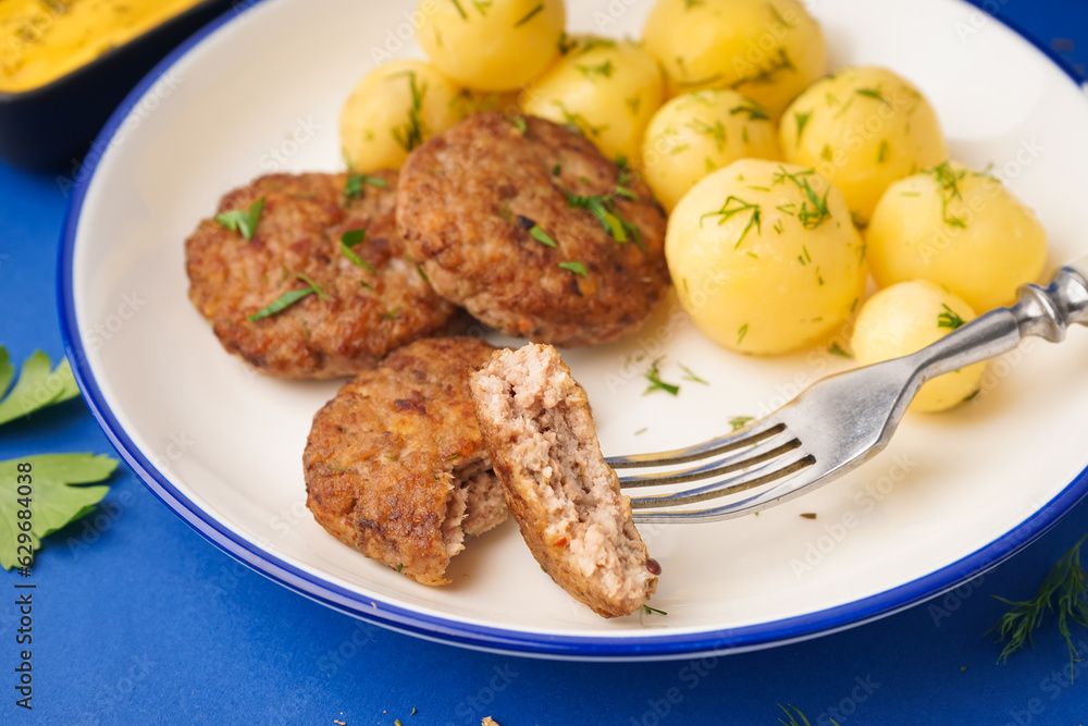 Plate with cutlets, boiled baby potatoes and dill on blue background