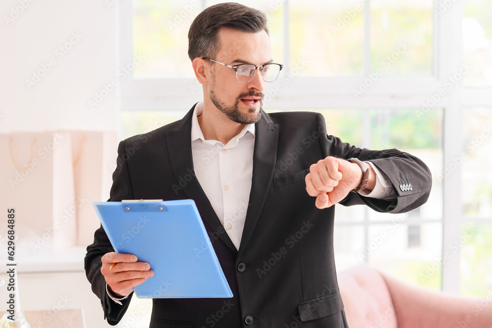 Male wedding planner with clipboard looking at wristwatch in office