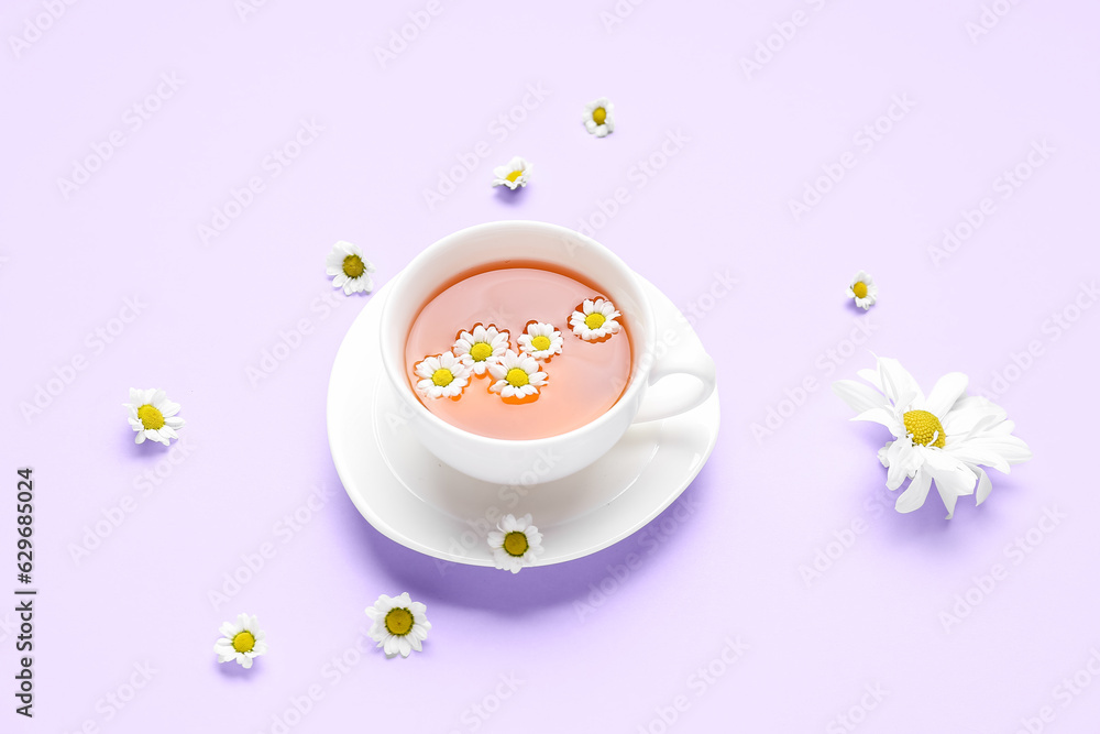 Cup of natural chamomile tea with flowers on lilac background