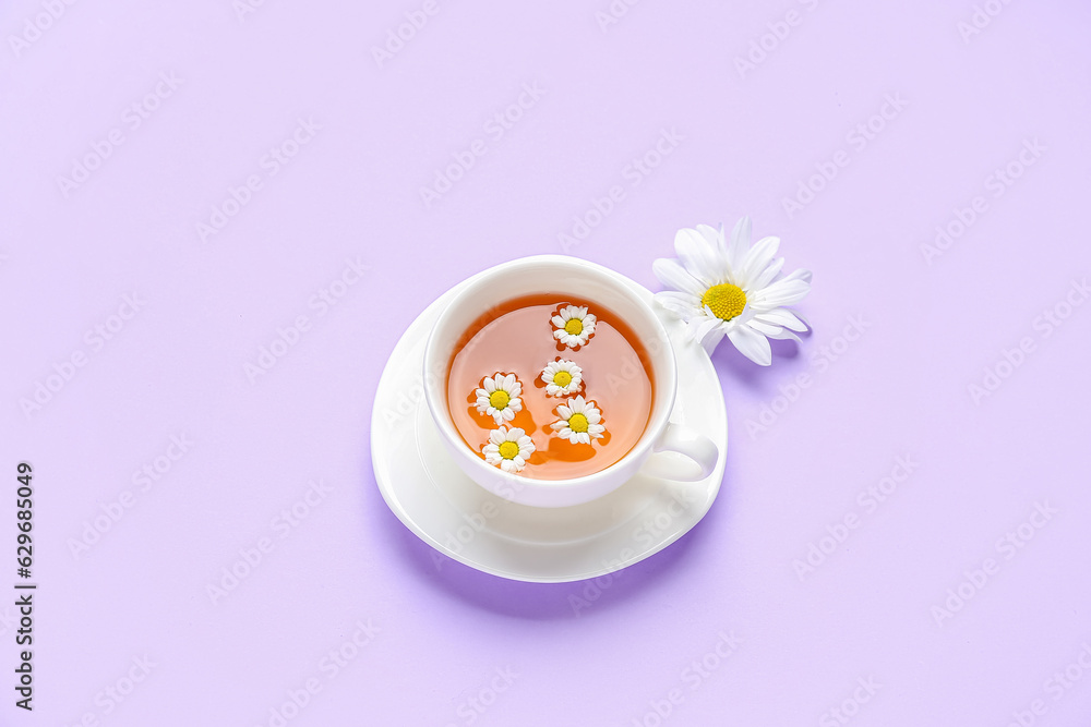 Cup of natural chamomile tea with flower on lilac background