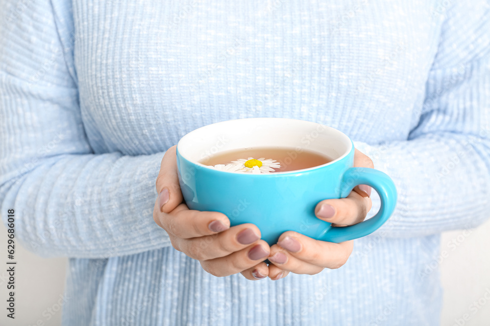 Beautiful young woman with cup of chamomile tea near white wall