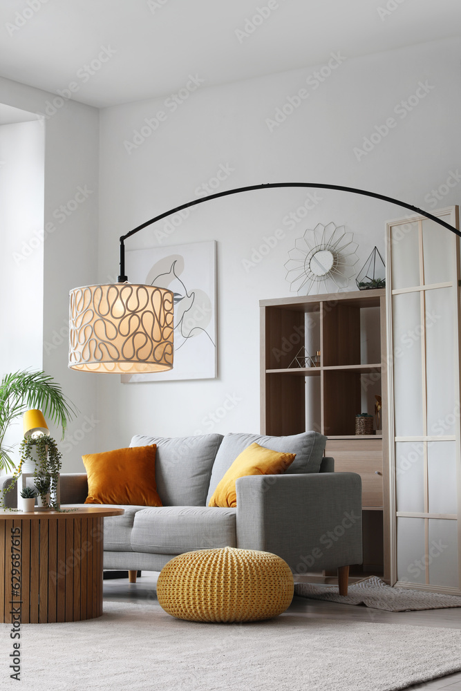 Interior of light living room with cozy grey sofa, coffee table and glowing lamps