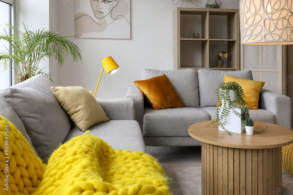 Interior of light living room with cozy grey sofa, coffee table and glowing lamps