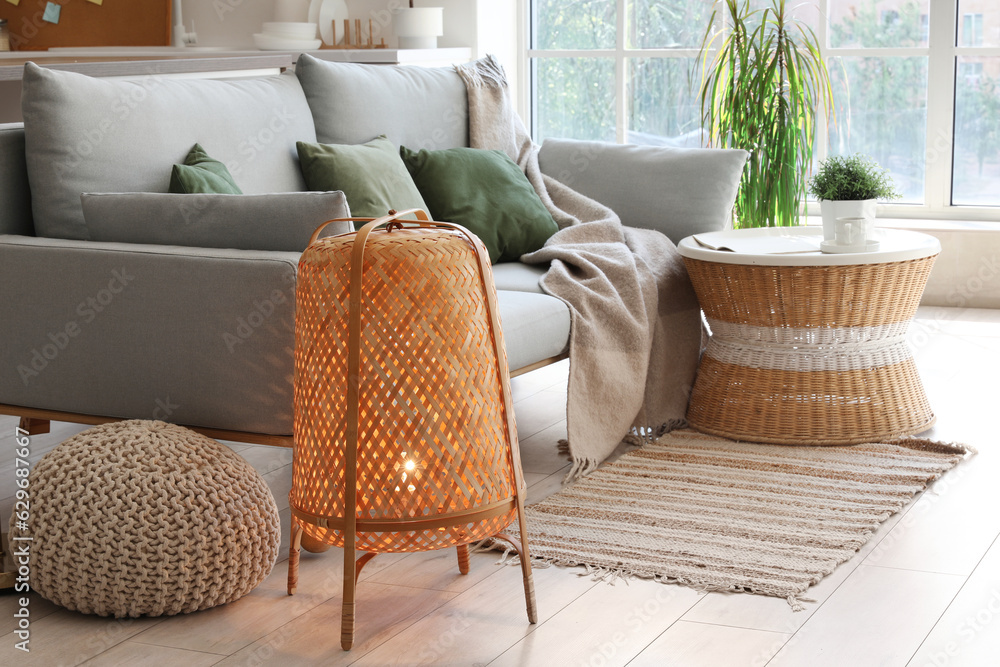 Interior of light living room with cozy grey sofa, coffee table and glowing lamp