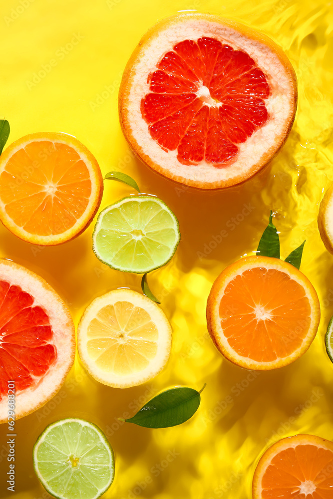 Different citrus fruit slices and leaves in water on yellow background