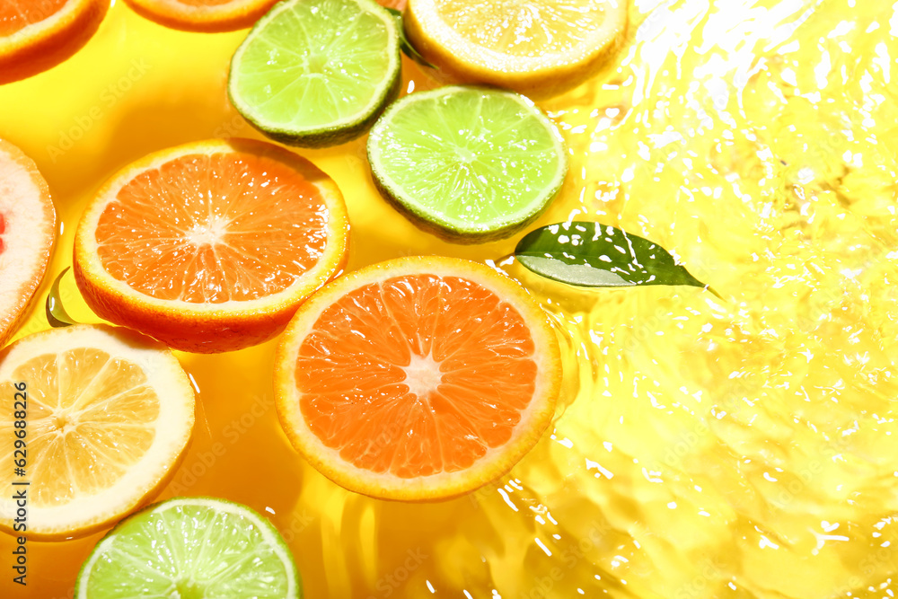 Different citrus fruit slices and leaves in water on yellow background