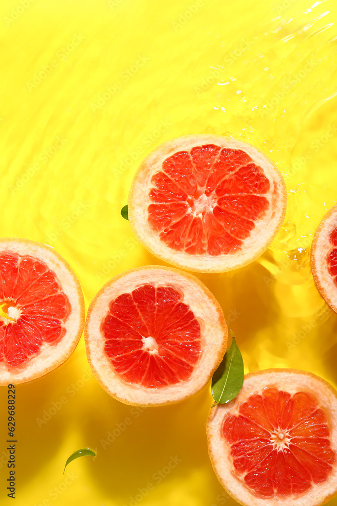 Slices of fresh grapefruit and leaves in water on yellow background