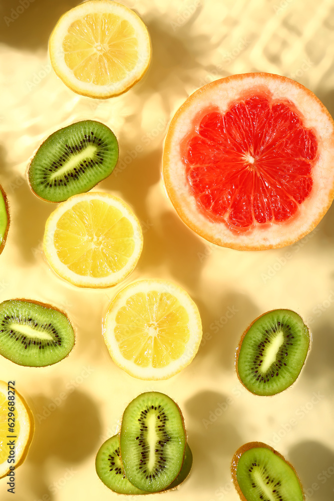 Different fruit slices in water on yellow background