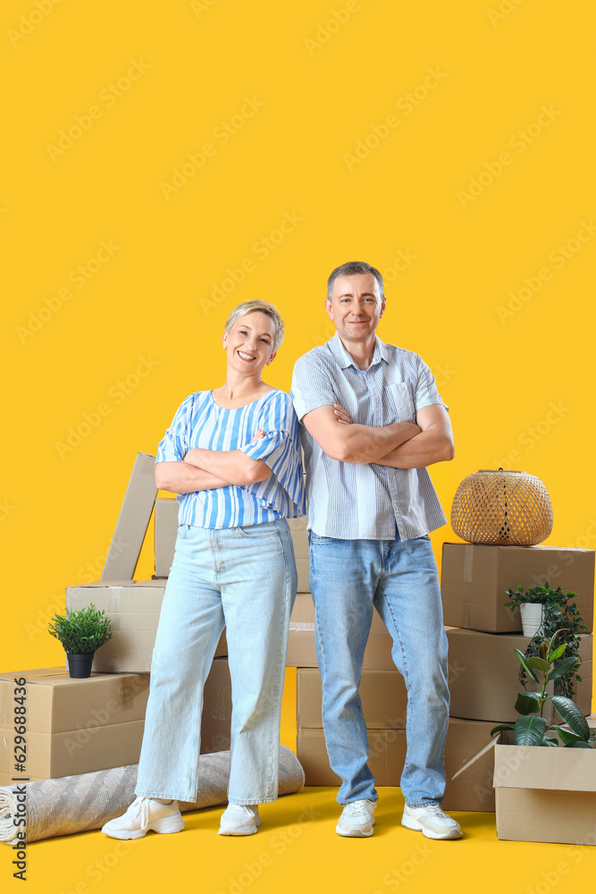 Mature couple with moving boxes on yellow background