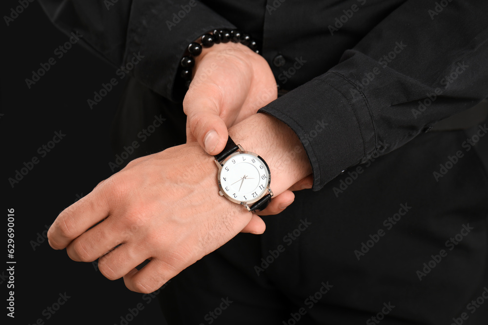 Elegant young man looking at wristwatch on black background, closeup