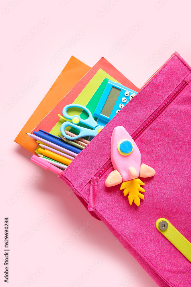 Backpack with rocket made of plasticine and stationery on pink background