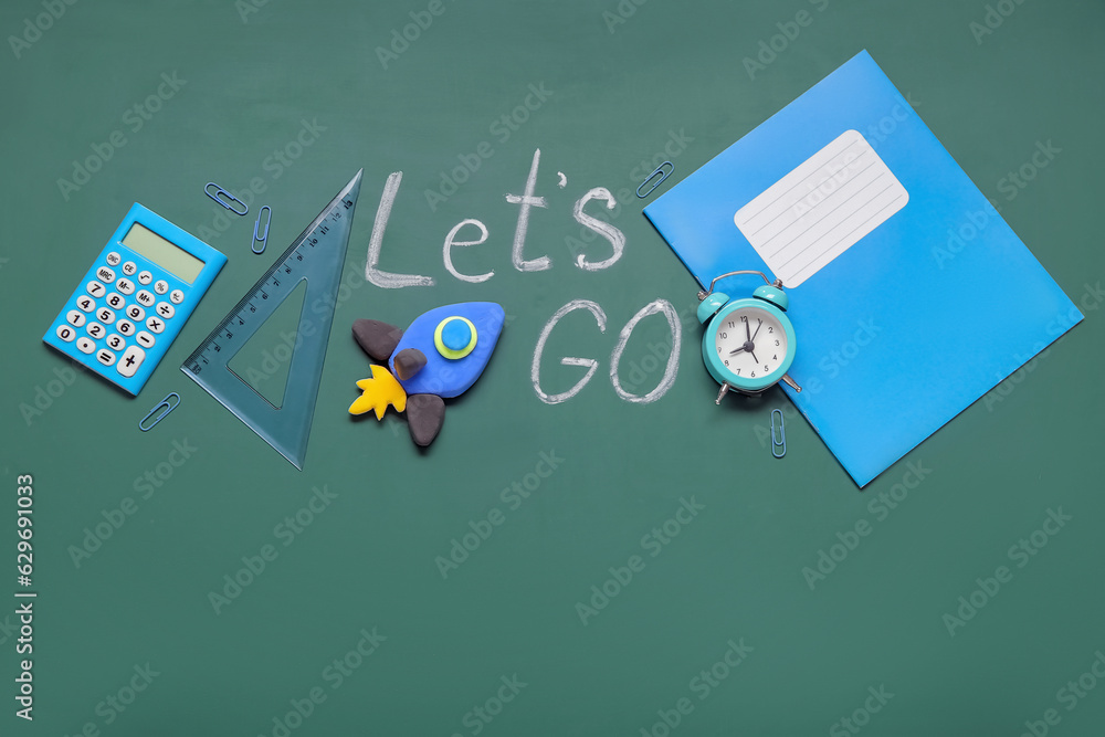 Rocket made of plasticine with different stationery and text LETS GO on green chalkboard