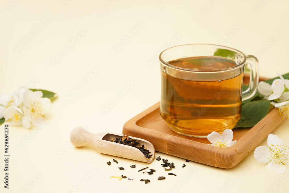 Cup of aromatic tea, dried leaves and beautiful jasmine flowers on color background