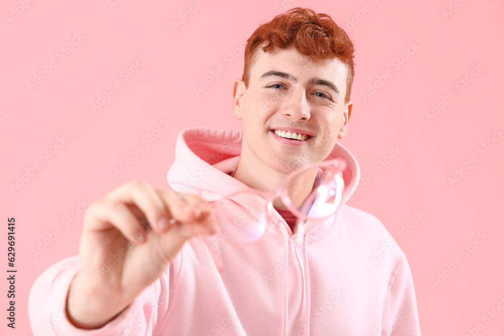 Young redhead man with eyeglasses on pink background, closeup