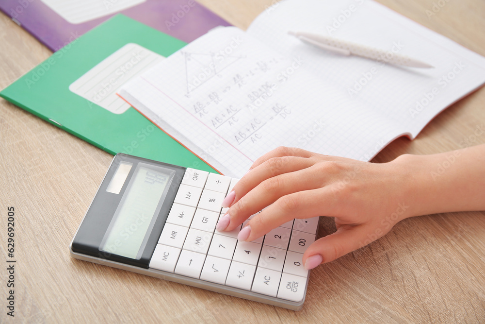 Woman working with calculator on wooden table, closeup