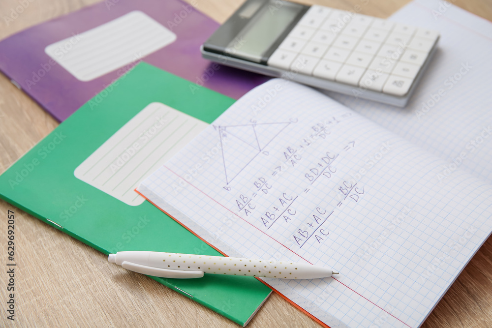 Open copybook with formulas, calculator and pen on wooden table