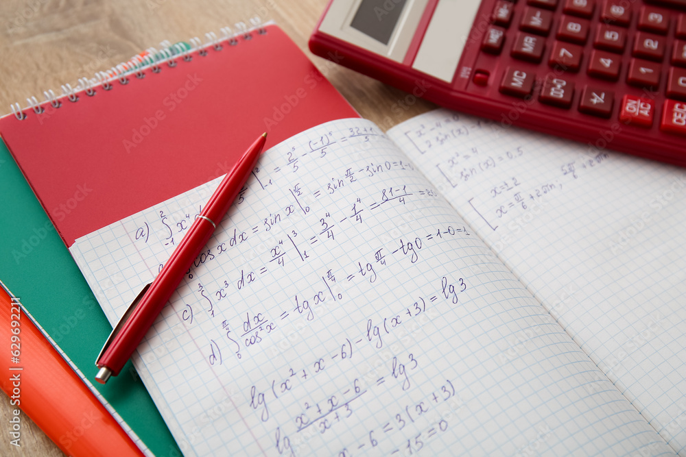 Open copybook with math formulas and pen on wooden table, closeup