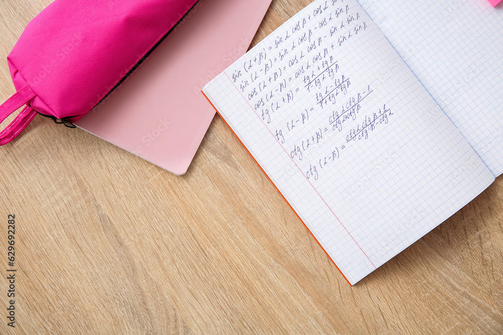 Open copybook with math formulas on wooden table