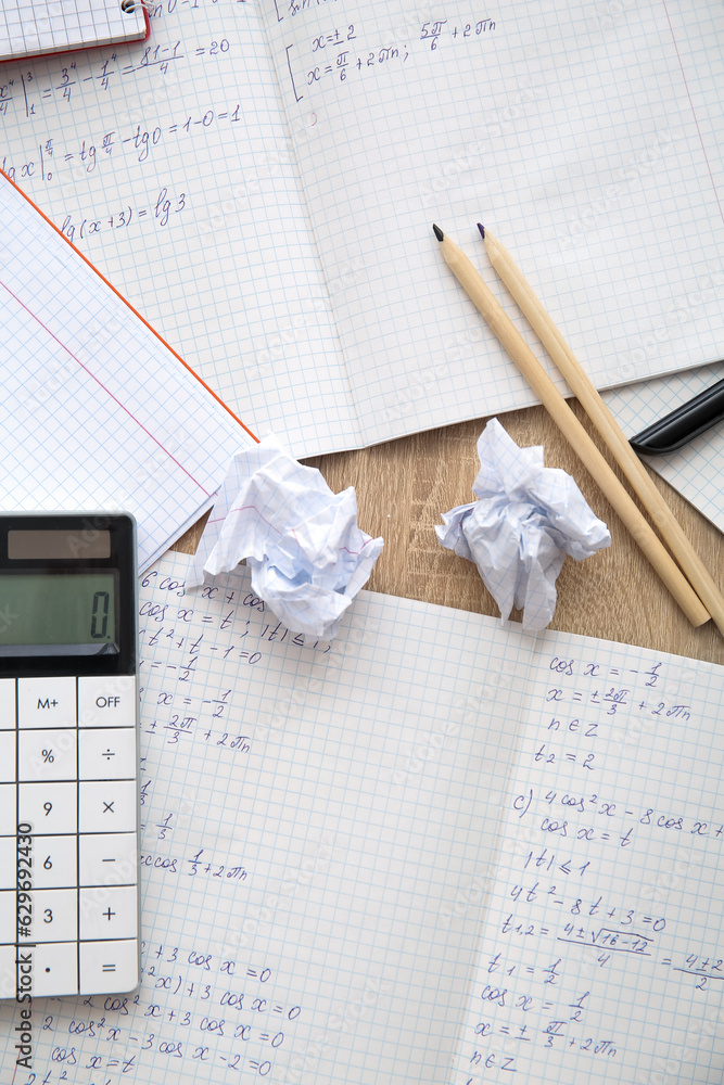 Copybooks with math formulas, crumbled paper and calculator on wooden table