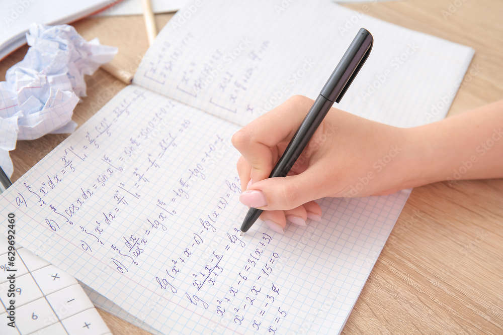 Woman writing math formulas in copybook on wooden table