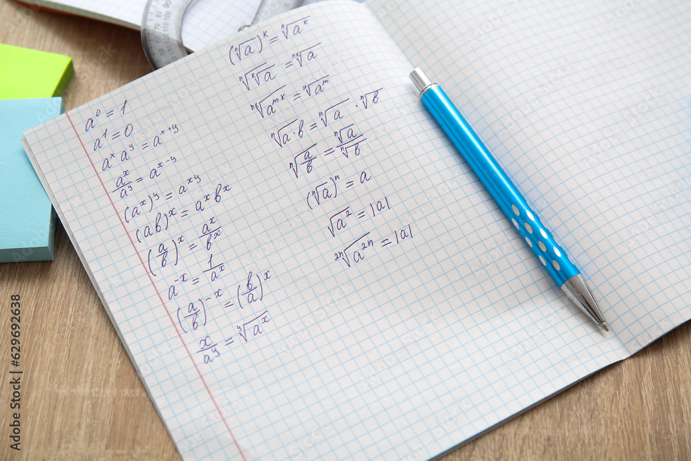 Open copybook with math formulas and pen on wooden table, closeup