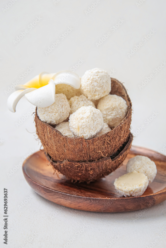 Coconut shell with white chocolate candies and plumeria flower on light table