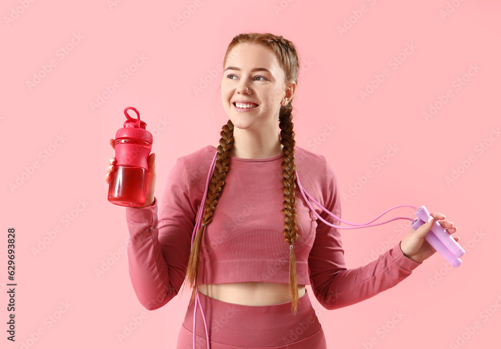 Sporty young woman with skipping rope and bottle of water on pink background