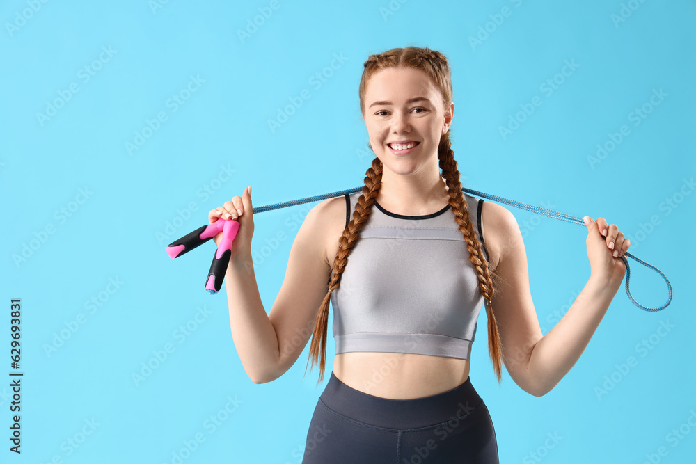 Sporty young woman with skipping rope on blue background